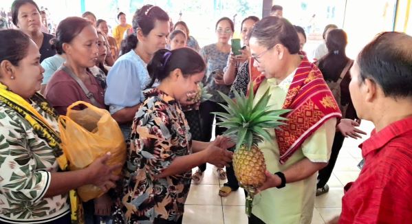 Puluhan ibu-ibu berdiri berbaris sambil menenteng hasil kebun mereka