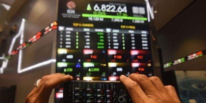 Seorang pengunjung sedang memotret indeks harga saham yang terpampang di papan elektronik di Gedung Bursa Efek Indonesia.