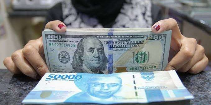 Pegawai tempat penukaran valas menunjukkan uang rupiah dan uang dolar AS