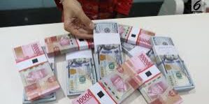 Seorang pegawai tempat penukaran valas menunjukkan lembaran uang rupiah di antara uang dolar AS.