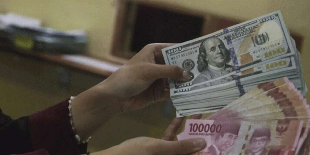 Pegawai tempat penukaran valas sedang menghitung lembaran uang dolar AS di antara lembaran uang rupiah