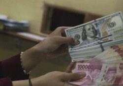 Petugas tempat penukaran valas sedang menunjukkan lembaran uang dolar AS di antara lembaran uang rupiah