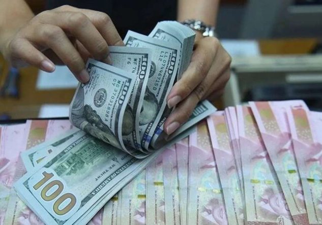 Pegawai tempat penukaran valas sedang menghitung lembaran uang dolar AS di antara lembaran uang rupiah