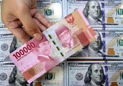 Seorang petugas memegang uang rupiah di atas tumpukan uang dolar AS, di tempat penukaran valuta asing.