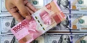 Seorang petugas memegang uang rupiah di atas tumpukan uang dolar AS, di tempat penukaran valuta asing.